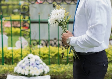 Man am Grab mit Blumen in der Hand